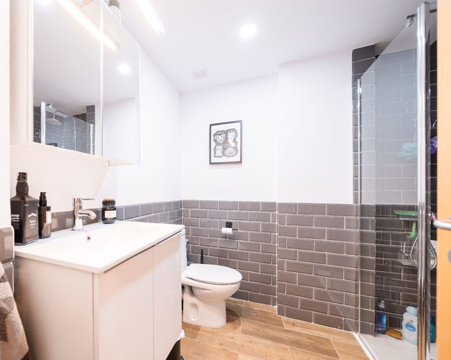 Baño con ducha y revestimiento cerámico gris en vivienda reformada
