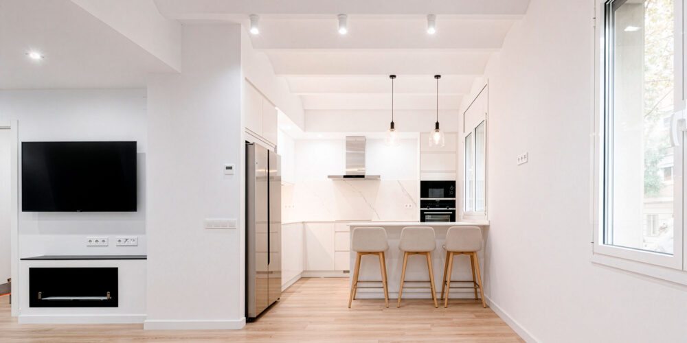 Cocina abierta blanca con isla y zona de estar en vivienda reformada