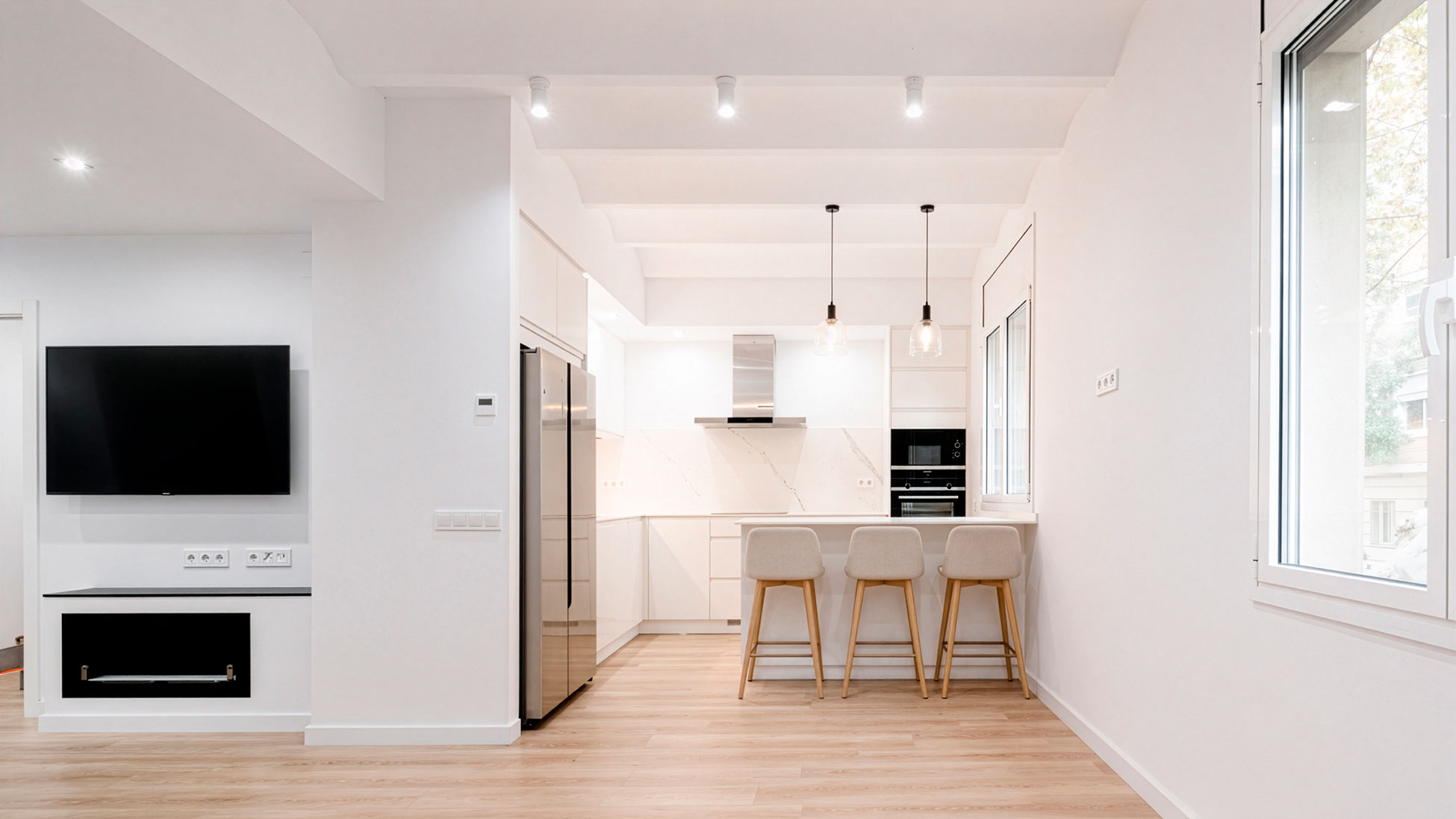 Cocina abierta blanca con isla y zona de estar en vivienda reformada