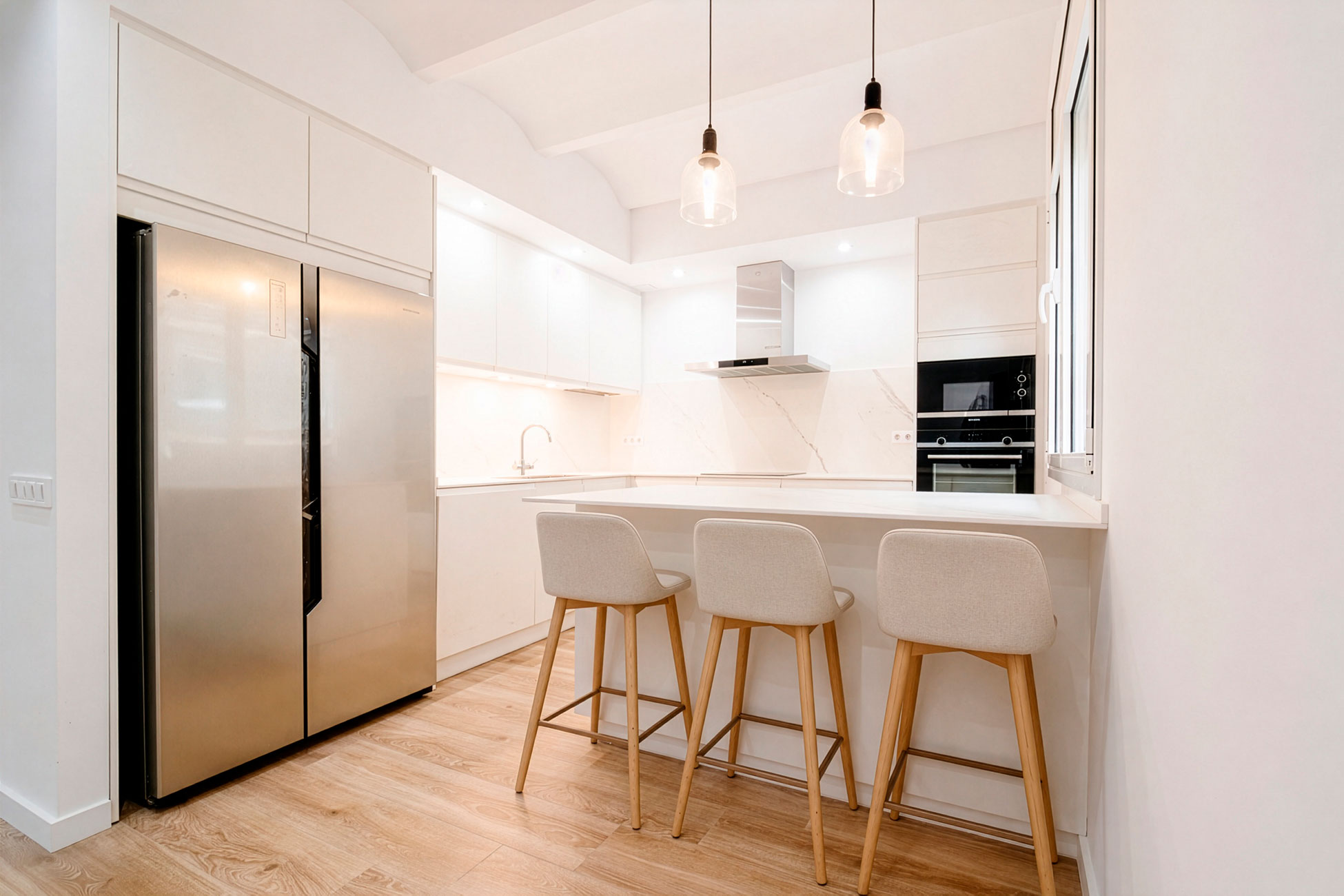 Cocina blanca con isla, taburetes y lámparas colgantes en Sarrià