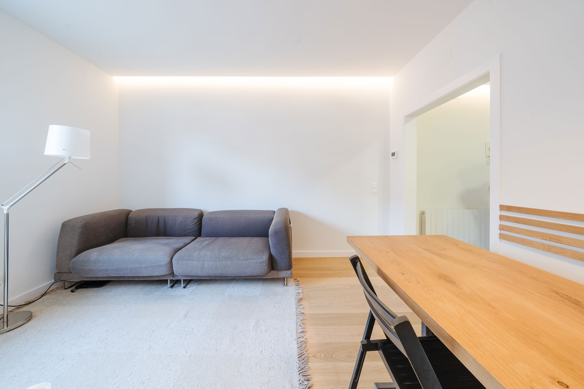 Salón comedor reformado en Barcelona con parqué de madera natural, paredes blancas, iluminación indirecta y mesa de comedor de madera