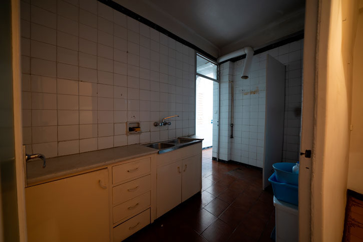 Cocina antigua y estrecha con mobiliario blanco, alicatado cerámico y salida a una galería.
