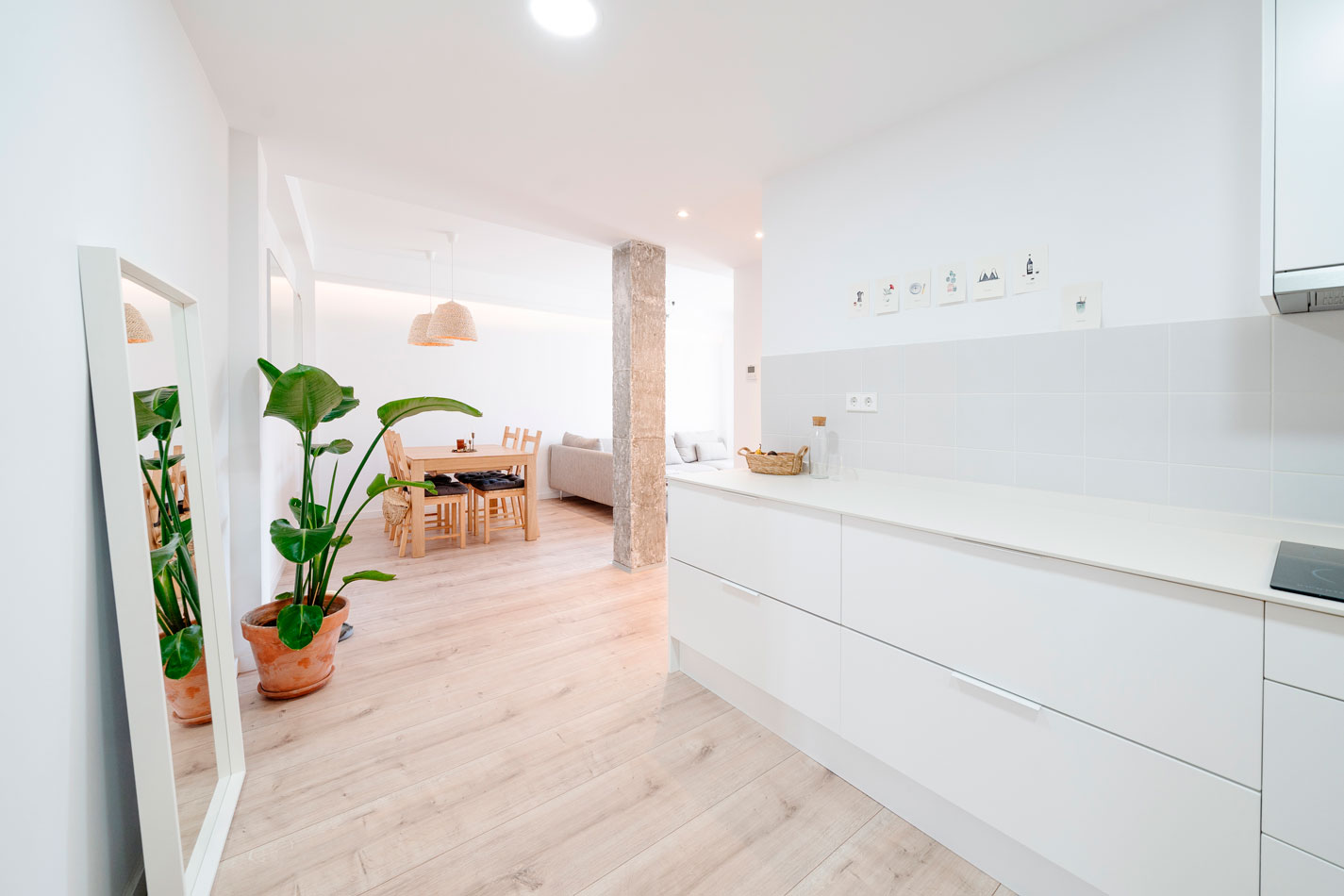Cocina abierta conectada con comedor y salón, con pavimento claro y pilar de hormigón visto.