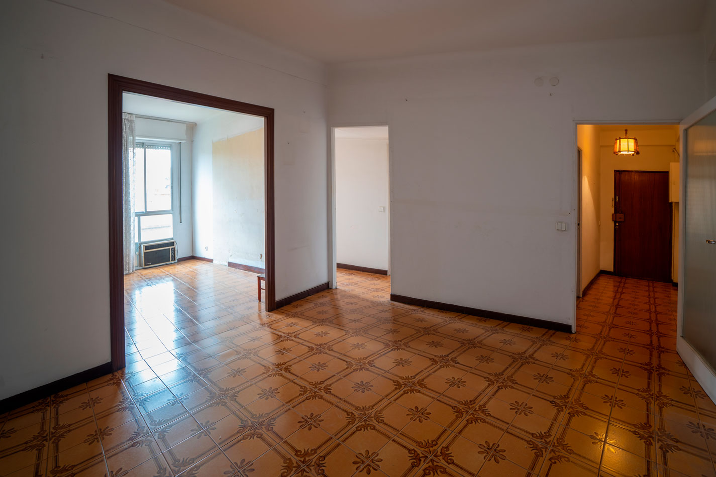 Interior del piso antes de la reforma, con suelo cerámico marrón, paredes divisorias y pasillo de entrada.