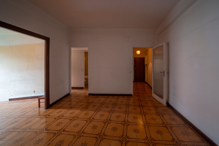 Zona de día antes de la reforma con paredes divisorias, pavimento marrón y habitaciones comunicadas.