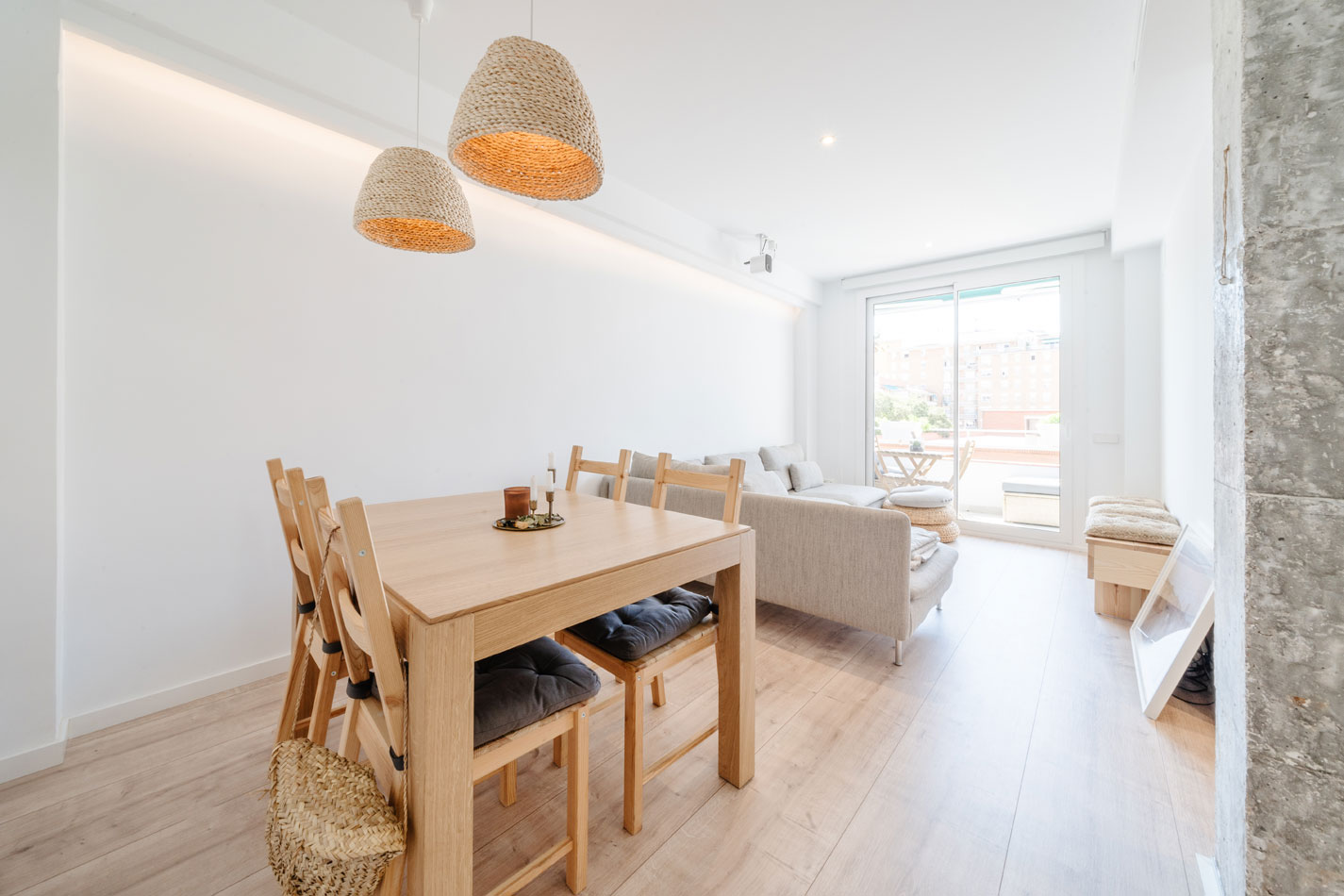 Comedor y salón abiertos con mesa de madera, lámparas de fibras naturales, sofá y salida a la terraza.