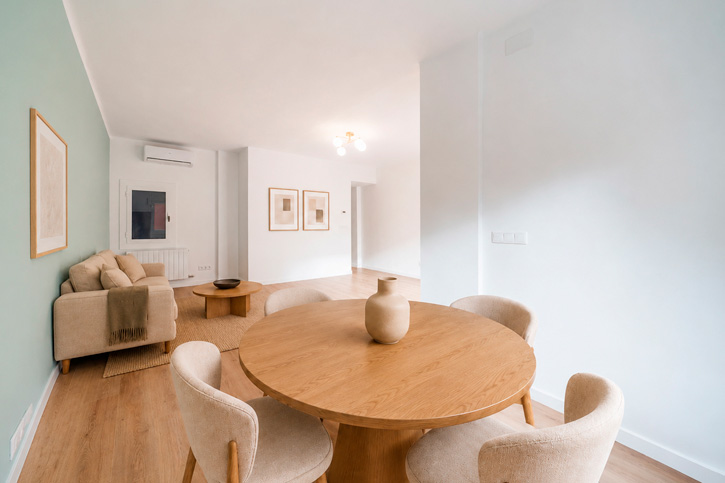 Comedor con mesa redonda de madera abierto al salón de una vivienda reformada en Barcelona.