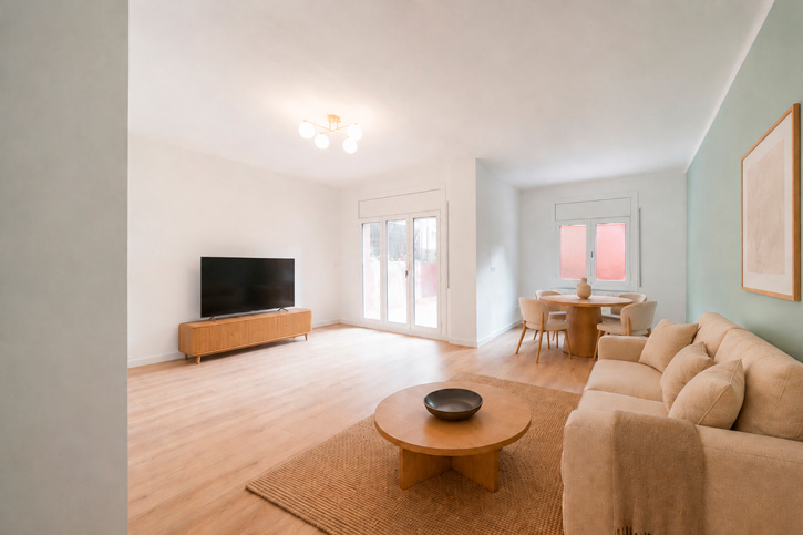 Salón-comedor reformado con suelo de madera, mobiliario neutro y acceso a una terraza.