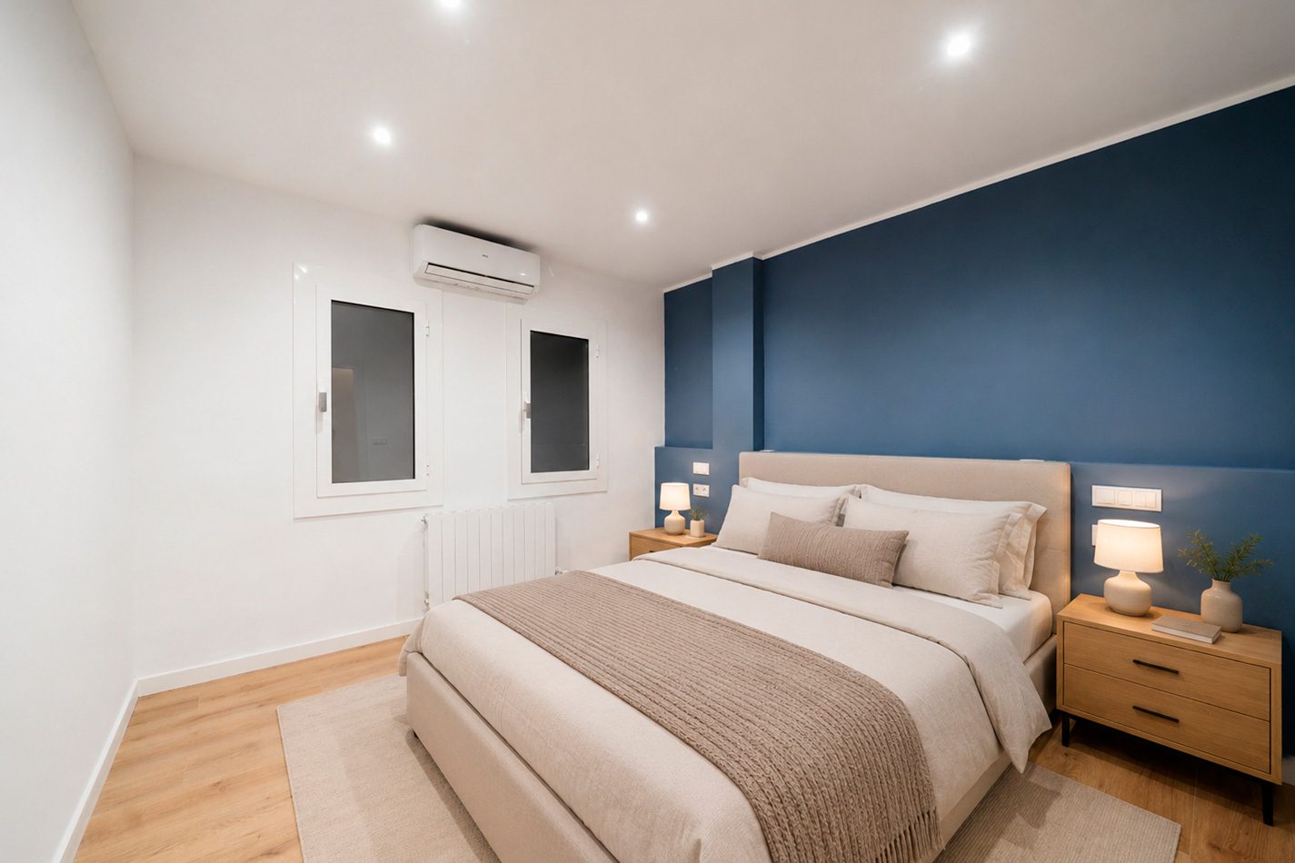 Dormitorio reformado con pared azul, cama tapizada y mobiliario de madera clara.