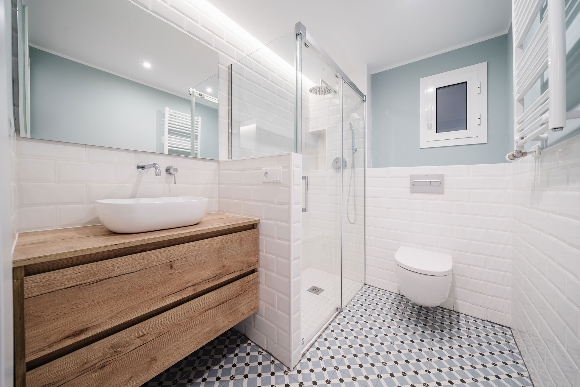 Baño reformado con mueble de madera y pavimento hidráulico en Barcelona.